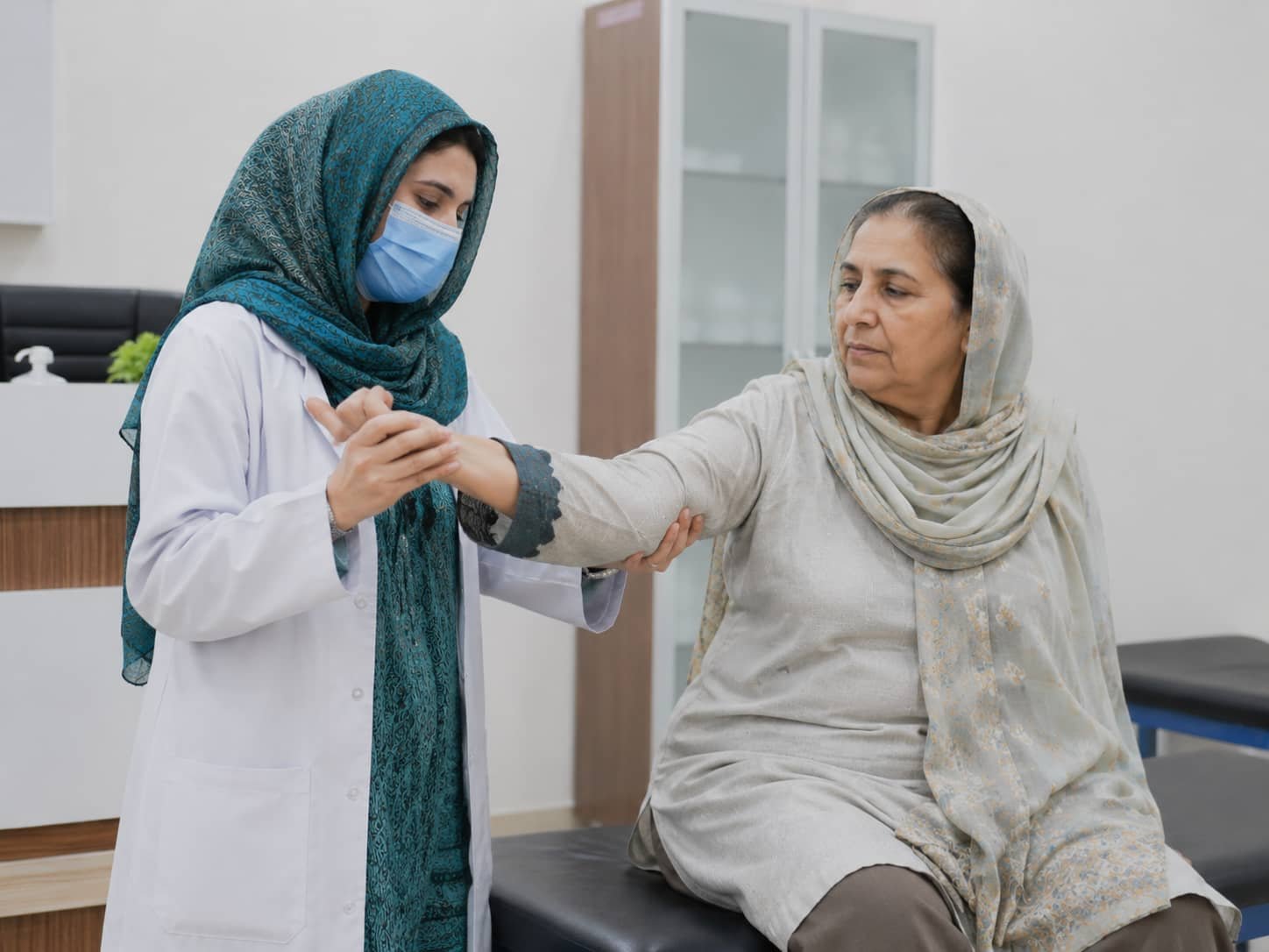 female physiotherapist helping an older female patient with arm and hand movement during arthritis physiotherapy