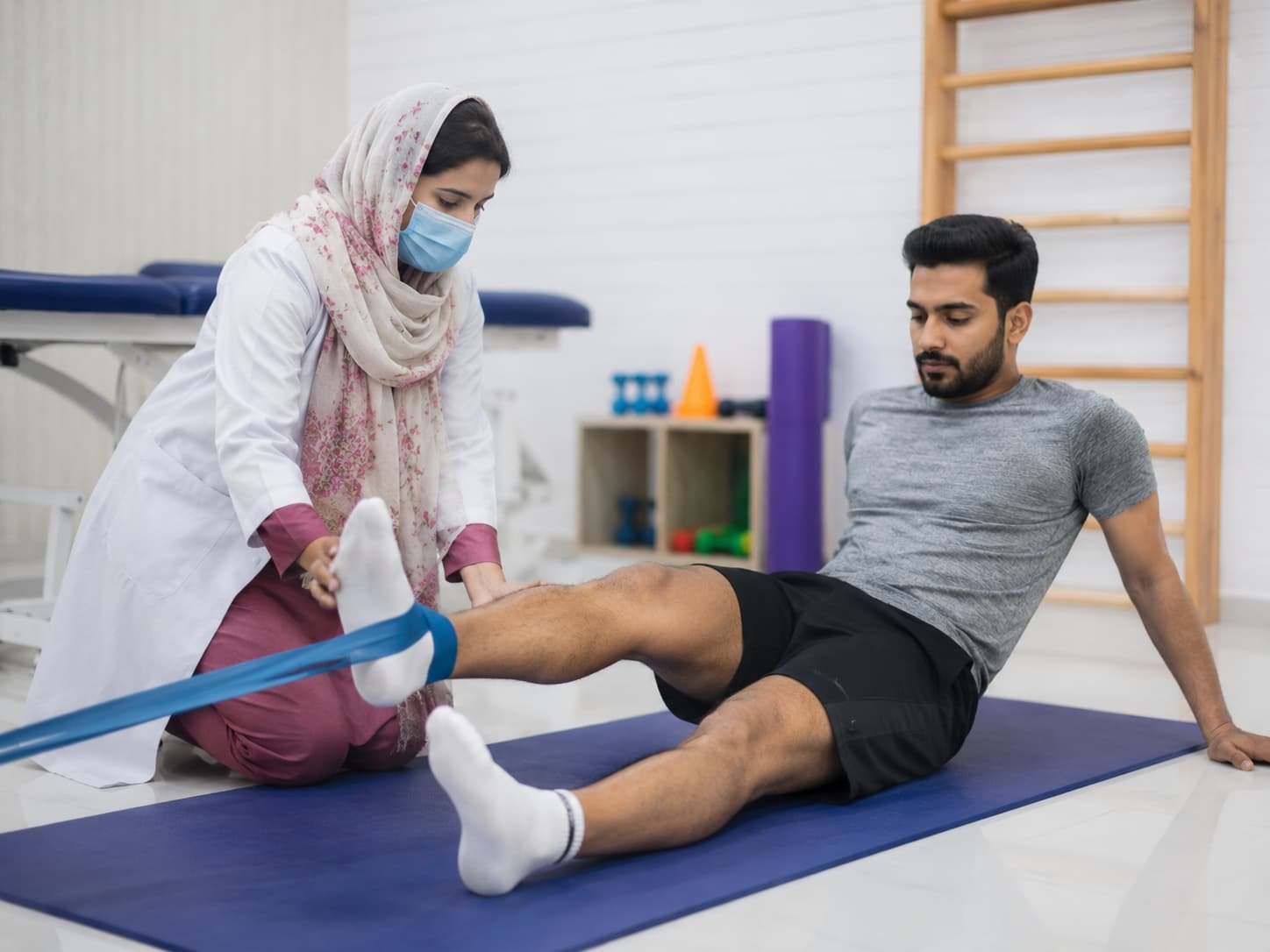 physiotherapist helping a male patient with a resistance band leg exercise during sports and injury rehabilitation