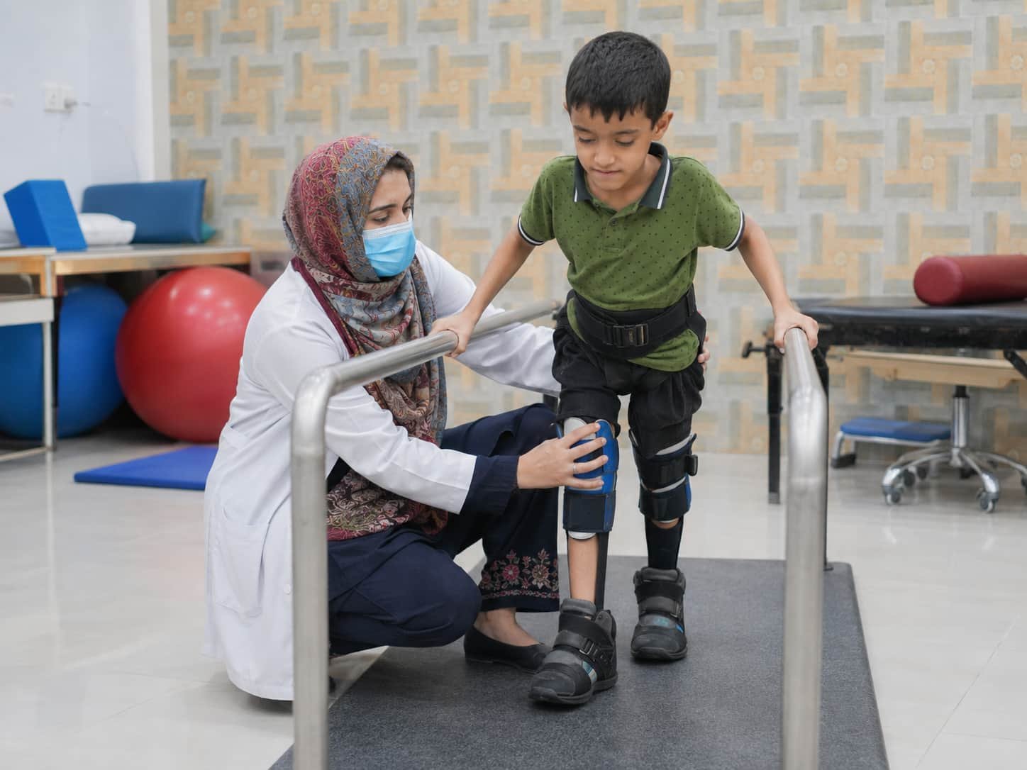 physiotherapist helping a young boy walk with leg supports and braces during cerebral palsy physiotherapy